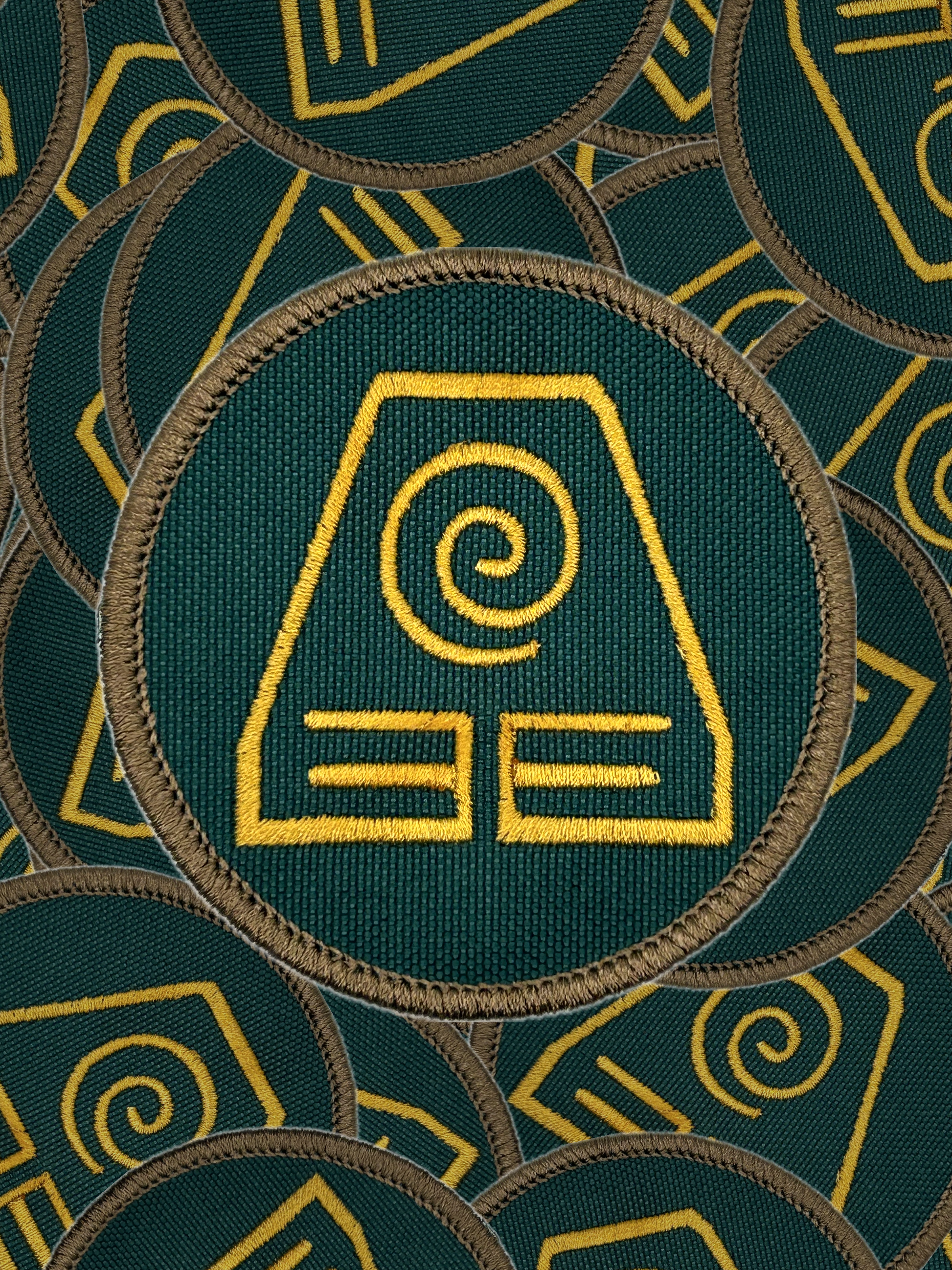 Green fabric with yellow earth bending embroidered patterns and symbols