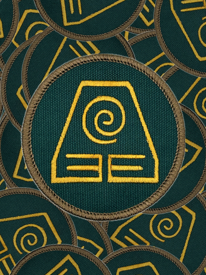 Green fabric with yellow earth bending embroidered patterns and symbols
