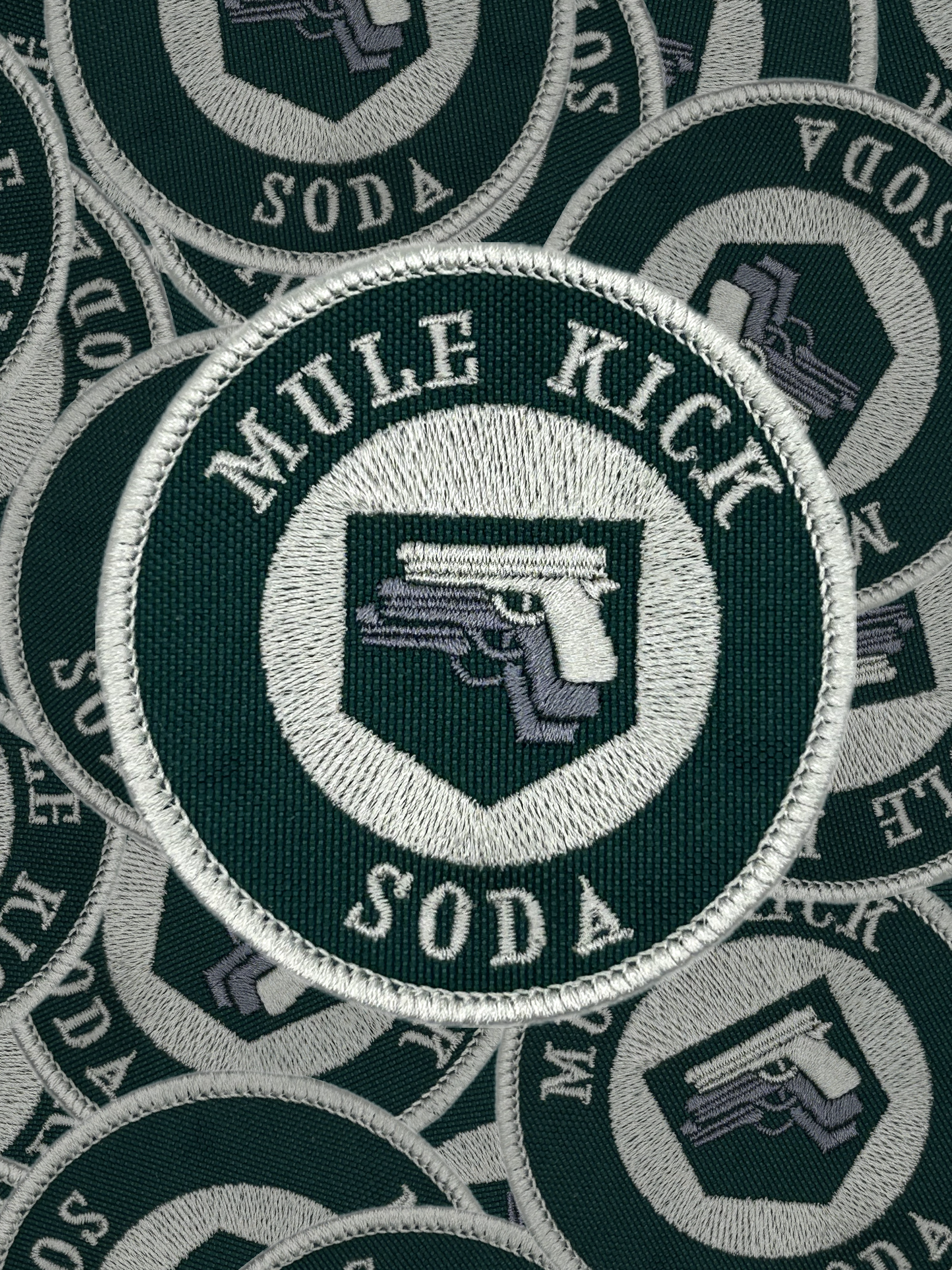Circular patch with 'Mule Kick Soda' text and logo on a green background, surrounded by similar patches.