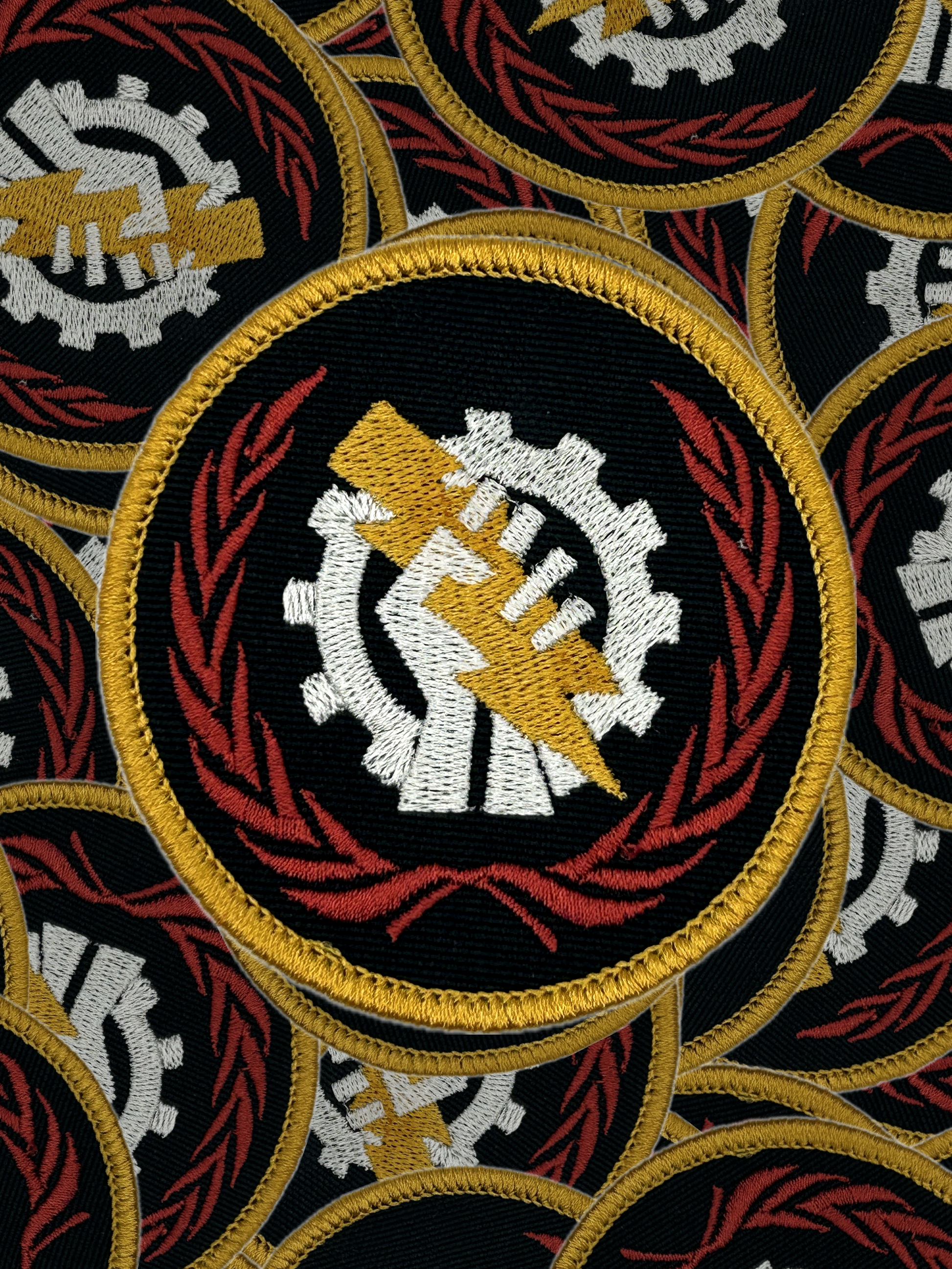 Pattern of embroidered patches with a Skitarii central design featuring a gear and a hand, surrounded by red and gold elements.