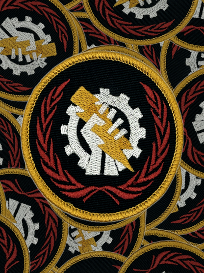 Pattern of embroidered patches with a Skitarii central design featuring a gear and a hand, surrounded by red and gold elements.