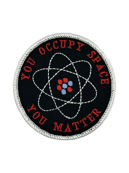 Round patch with atomic symbol and text 'YOU OCCUPY SPACE YOU MATTER' on a black background