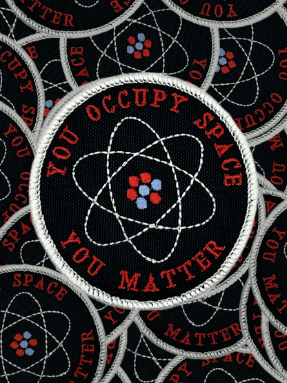 Patch with atomic design and text 'You Occupy Space You Matter' on a black background