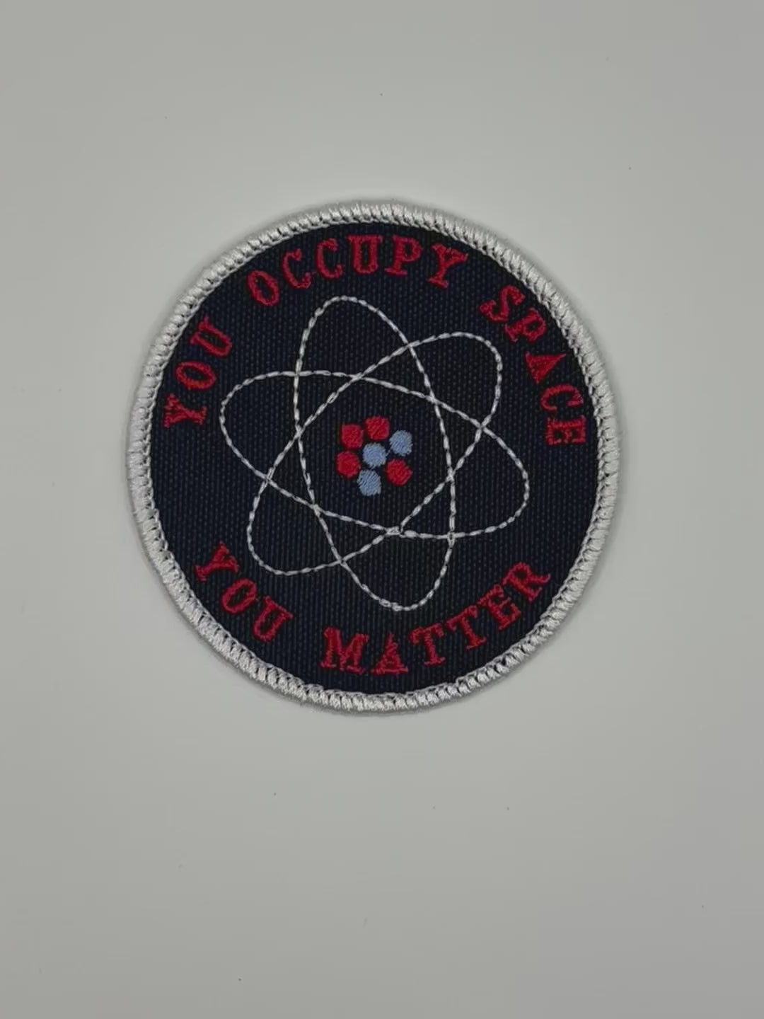 Round patch with atomic symbol and text 'YOU OCCUPY SPACE YOU MATTER' on a black background